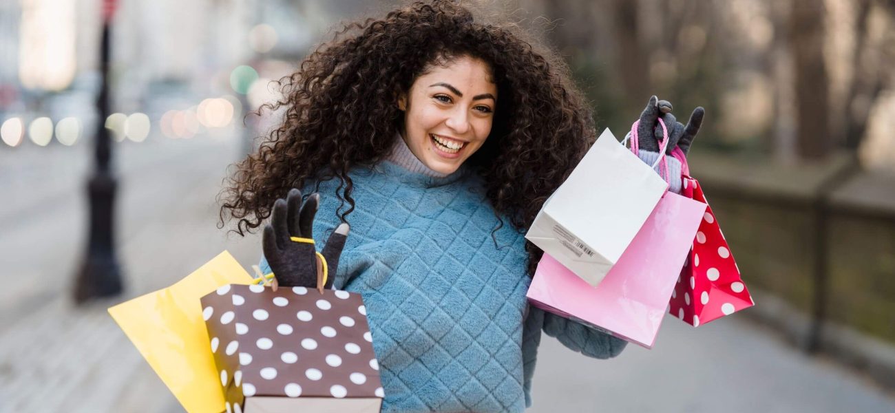 A smiling woman holding a selection of colourful shopping bags on a city street